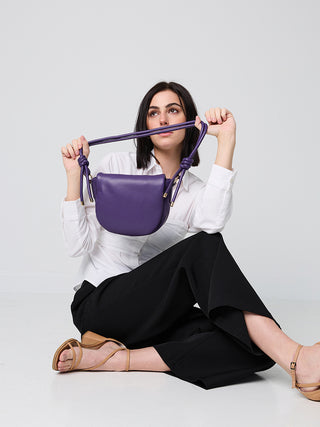 Dark Purple mini shoulder bag held by model, half-moon shape with twisted handles