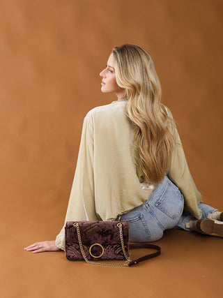 Chocolate velvet crossbody bag on a model with chain strap and circular ring closure