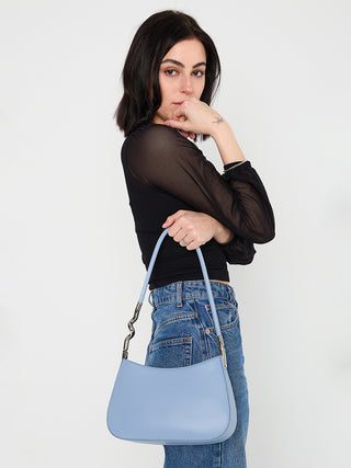 Light blue curved shoulder bag with chain strap, worn crossbody over denim