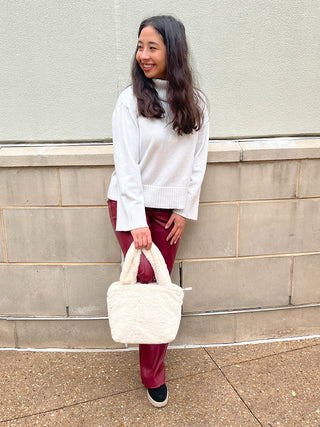 Off-white fuzzy satchel held by model, short handles and side straps