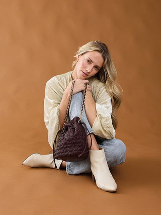 Ruched bucket bag in sangria (dark red) with chain strap, held by model