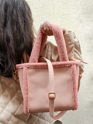 Pink sherpa-trim satchel held in hand, vegan leather-look body with adjustable strap